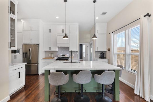 kitchen with stainless steel appliances, an island with sink, white cabinets, and decorative light fixtures