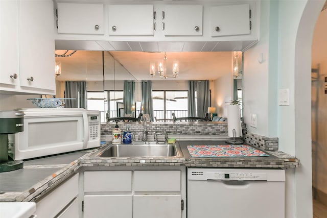 kitchen with white appliances, tasteful backsplash, an inviting chandelier, white cabinetry, and sink