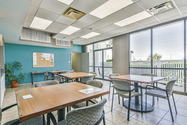 dining space featuring a drop ceiling, a wall of windows, and light tile patterned floors