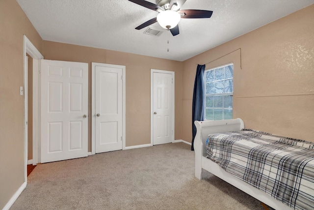 bedroom with light colored carpet, ceiling fan, a textured ceiling, and multiple closets