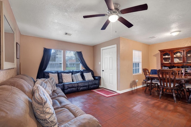 living room with a textured ceiling, ceiling fan, and a healthy amount of sunlight