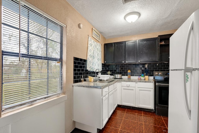 kitchen with stainless steel electric stove, sink, white cabinetry, white fridge, and backsplash