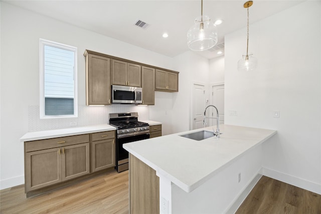 kitchen featuring kitchen peninsula, sink, hanging light fixtures, light wood-type flooring, and stainless steel appliances