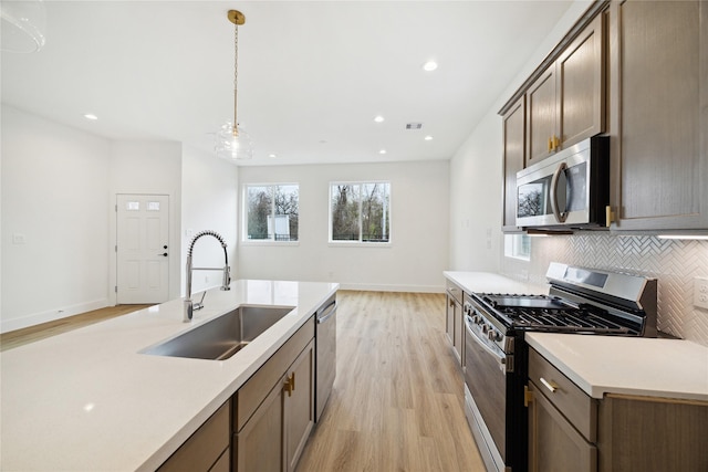 kitchen featuring pendant lighting, stainless steel appliances, tasteful backsplash, light hardwood / wood-style floors, and sink