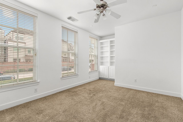 carpeted empty room with built in shelves, ceiling fan, and a healthy amount of sunlight