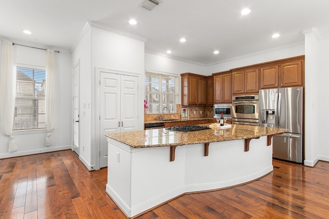 kitchen featuring light stone counters, a center island, a breakfast bar area, appliances with stainless steel finishes, and sink