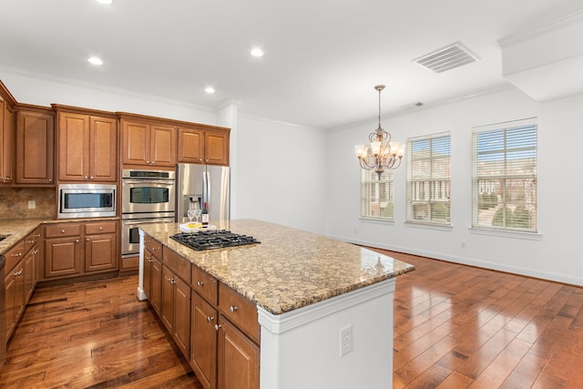 kitchen with appliances with stainless steel finishes, ornamental molding, dark hardwood / wood-style floors, a kitchen island, and an inviting chandelier