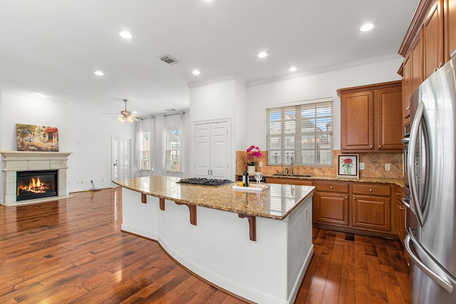 kitchen featuring stainless steel appliances, light stone countertops, a kitchen bar, a kitchen island, and sink