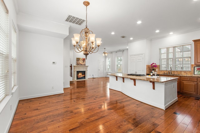 kitchen with light stone counters, a center island, hanging light fixtures, a breakfast bar area, and ornamental molding