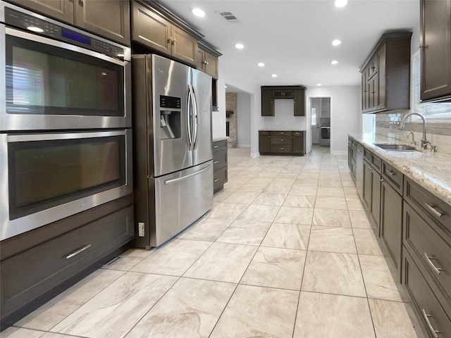 kitchen featuring appliances with stainless steel finishes, sink, light stone counters, and dark brown cabinets