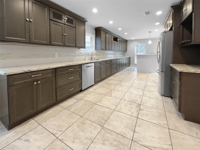 kitchen with appliances with stainless steel finishes, sink, light stone counters, and decorative light fixtures