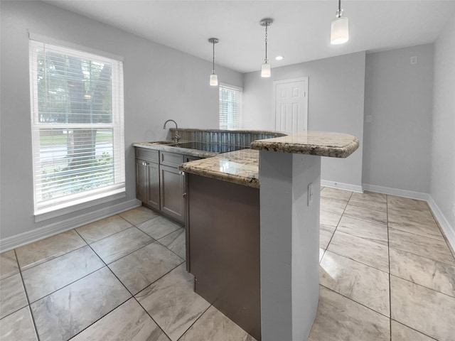 kitchen with decorative light fixtures, kitchen peninsula, stone counters, and a healthy amount of sunlight