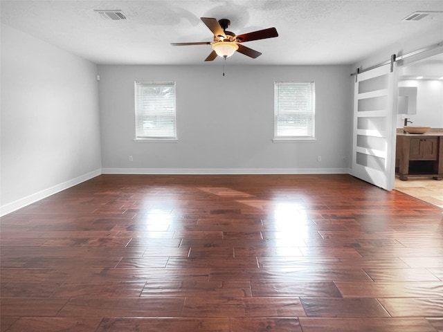 unfurnished living room featuring sink, dark hardwood / wood-style floors, a barn door, and a healthy amount of sunlight