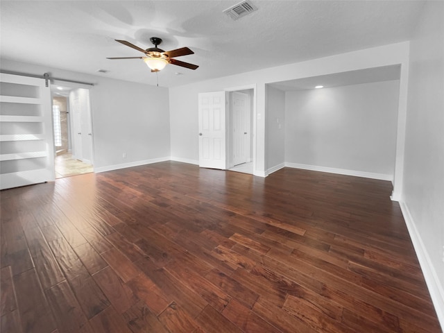 unfurnished living room with ceiling fan, dark hardwood / wood-style flooring, and a barn door