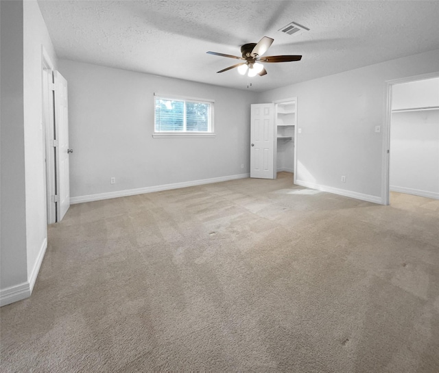 unfurnished bedroom featuring a spacious closet, a textured ceiling, a closet, ceiling fan, and light colored carpet