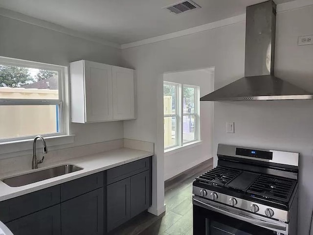 kitchen featuring sink, stainless steel range with gas cooktop, white cabinets, wall chimney range hood, and crown molding