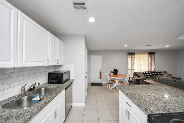 kitchen featuring dishwasher, dark stone countertops, sink, light tile patterned floors, and white cabinets