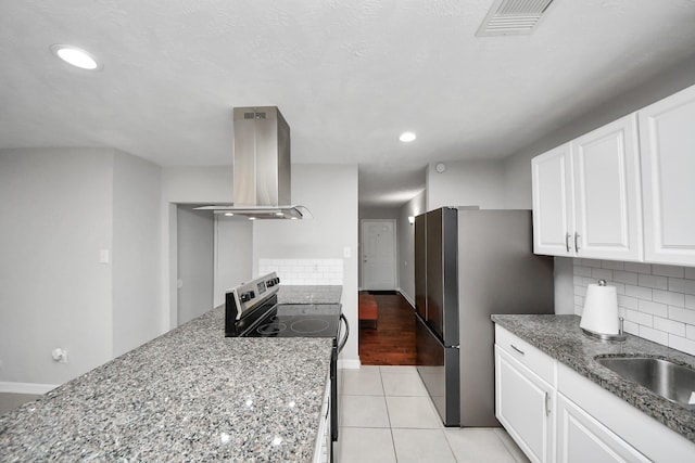 kitchen with electric stove, backsplash, island exhaust hood, white cabinetry, and light tile patterned floors