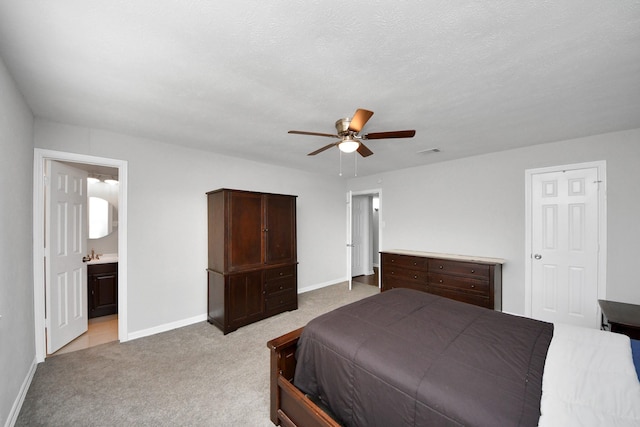 bedroom with ceiling fan, light colored carpet, ensuite bathroom, and a textured ceiling