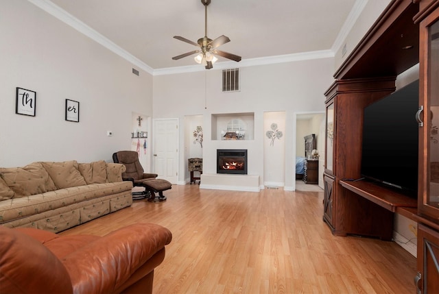 living room with a high ceiling, ceiling fan, crown molding, and light hardwood / wood-style floors