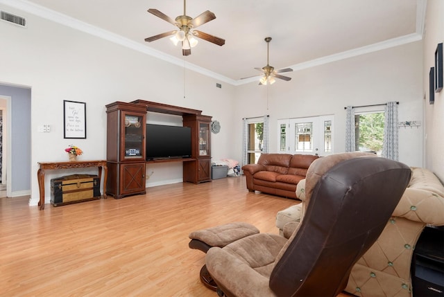 living room featuring a towering ceiling, ceiling fan, crown molding, and light wood-type flooring