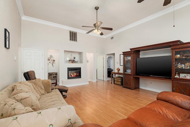 living room featuring a towering ceiling, wood-type flooring, ceiling fan, and crown molding