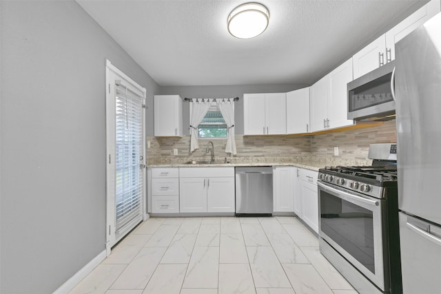 kitchen with stainless steel appliances, sink, white cabinets, backsplash, and light stone countertops