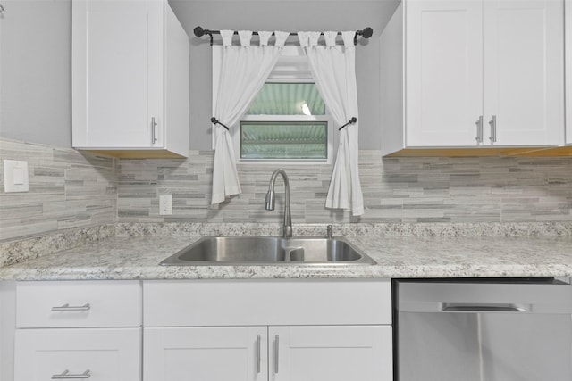 kitchen with stainless steel dishwasher, white cabinetry, sink, and backsplash