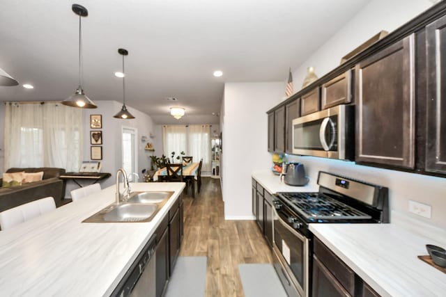 kitchen featuring pendant lighting, light hardwood / wood-style floors, appliances with stainless steel finishes, dark brown cabinets, and sink