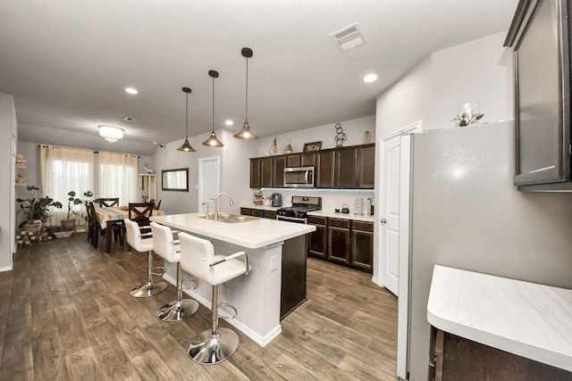 kitchen with stainless steel appliances, sink, decorative light fixtures, an island with sink, and wood-type flooring