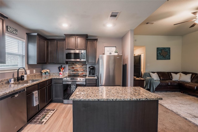 kitchen with light stone counters, sink, a center island, and stainless steel appliances