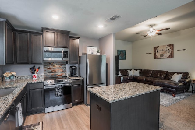 kitchen featuring light wood-type flooring, a center island, light stone countertops, and appliances with stainless steel finishes