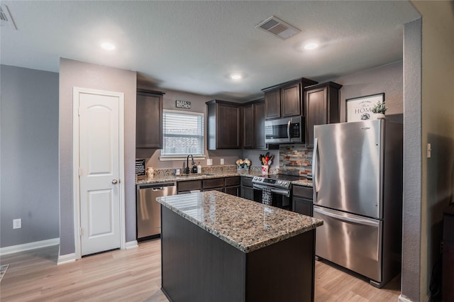 kitchen featuring light stone countertops, dark brown cabinetry, a center island, stainless steel appliances, and sink