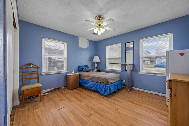 bedroom with white refrigerator, light wood-type flooring, ceiling fan, and a textured ceiling