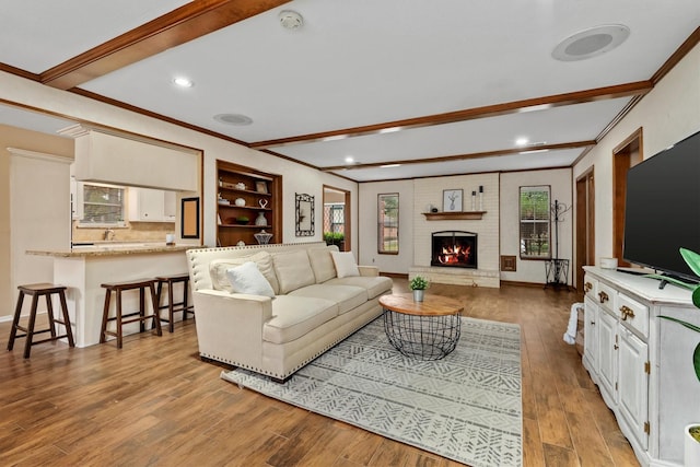 living room with a fireplace, light hardwood / wood-style floors, beamed ceiling, and ornamental molding