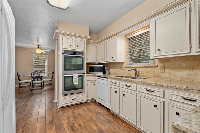 kitchen with appliances with stainless steel finishes, light stone countertops, ceiling fan, dark wood-type flooring, and sink