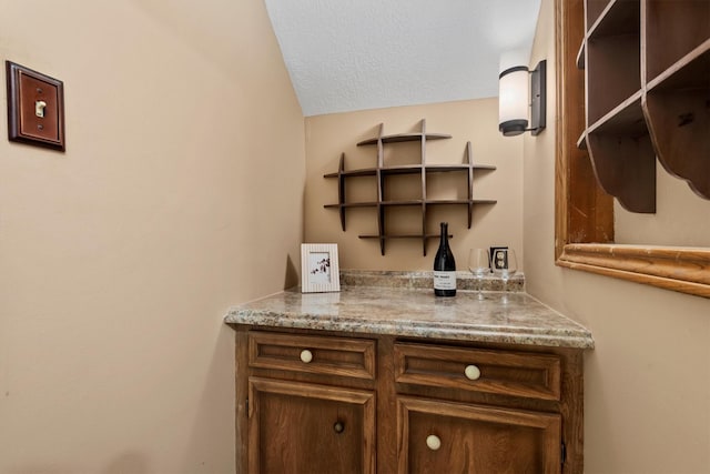 bar featuring stone counters and a textured ceiling