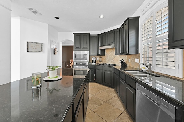 kitchen with tasteful backsplash, appliances with stainless steel finishes, sink, and dark stone countertops