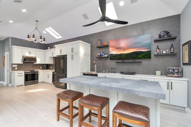 kitchen with appliances with stainless steel finishes, ceiling fan, pendant lighting, lofted ceiling with skylight, and white cabinetry