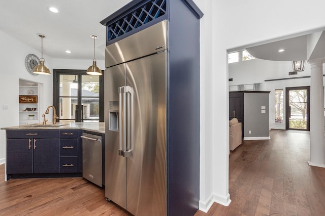 kitchen featuring ornate columns, stainless steel built in refrigerator, light stone countertops, dark hardwood / wood-style flooring, and sink