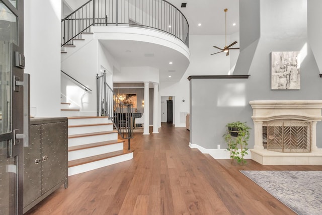 entryway with ornate columns, wood-type flooring, a towering ceiling, ceiling fan, and a fireplace