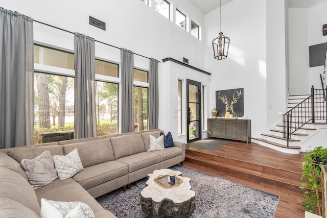 living room featuring a towering ceiling, wood-type flooring, a healthy amount of sunlight, and a notable chandelier