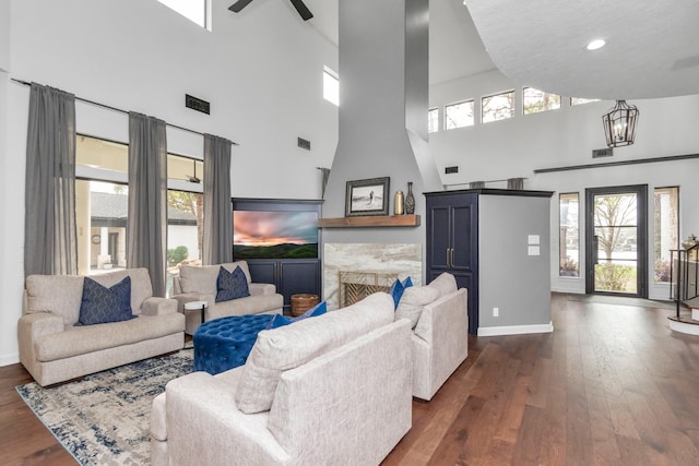 living room featuring ceiling fan with notable chandelier, a high ceiling, dark hardwood / wood-style flooring, and a fireplace