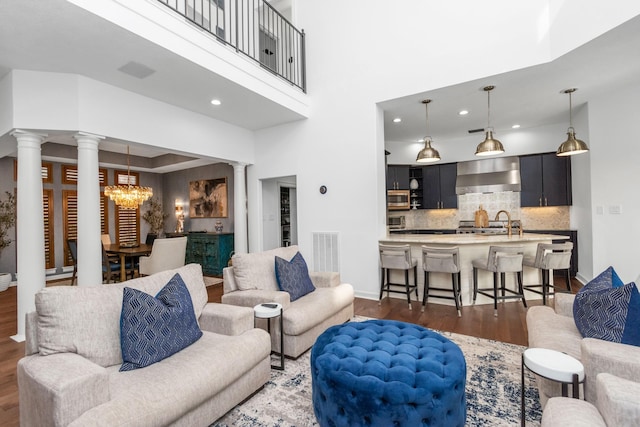 living room featuring sink, dark wood-type flooring, a chandelier, and a high ceiling