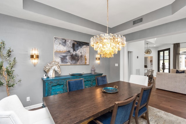 dining area featuring french doors, wood-type flooring, an inviting chandelier, and a tray ceiling