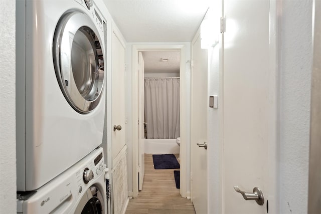 washroom with stacked washer and dryer, a textured ceiling, and light hardwood / wood-style floors