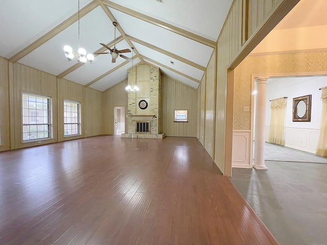 unfurnished living room featuring ornate columns, a brick fireplace, wood-type flooring, ceiling fan with notable chandelier, and beamed ceiling