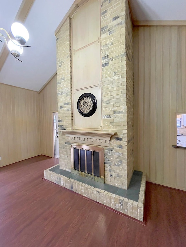 unfurnished living room with a brick fireplace, hardwood / wood-style floors, lofted ceiling, and wood walls