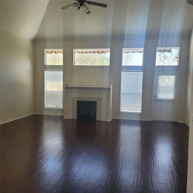 unfurnished living room with ceiling fan, dark wood-type flooring, a wealth of natural light, and high vaulted ceiling