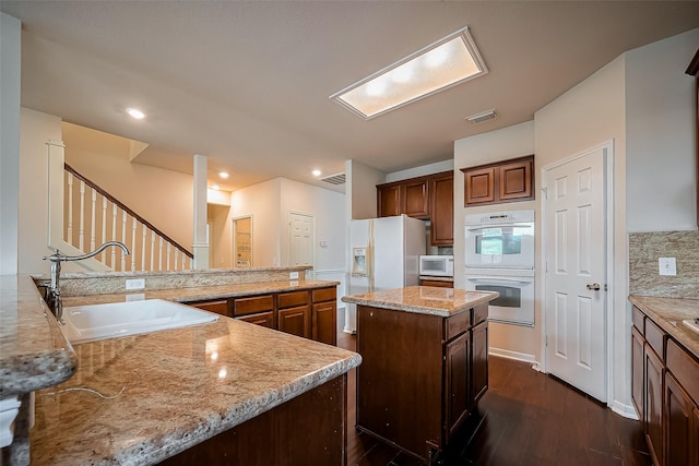 kitchen with visible vents, a center island, dark wood-style floors, white appliances, and a sink